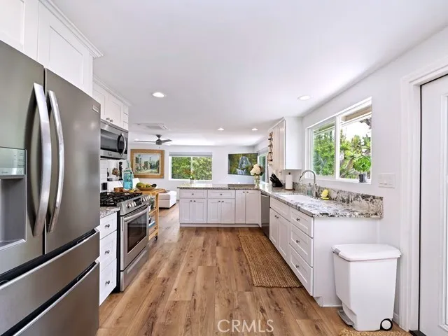 a kitchen with stainless steel appliances granite countertop a refrigerator a sink dishwasher a stove and white countertops with wooden floor