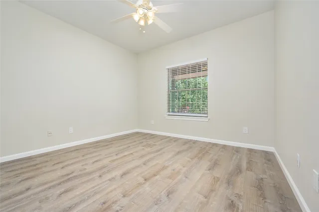 an empty room with wooden floor chandelier fan and windows