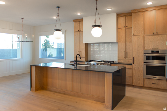 4658 South 380 East Washington, UT 84780 - Photo 8 of 10 Kitchen featuring dark stone counters, light wood finished floors, a kitchen island with sink, stainless steel double oven, and wood walls