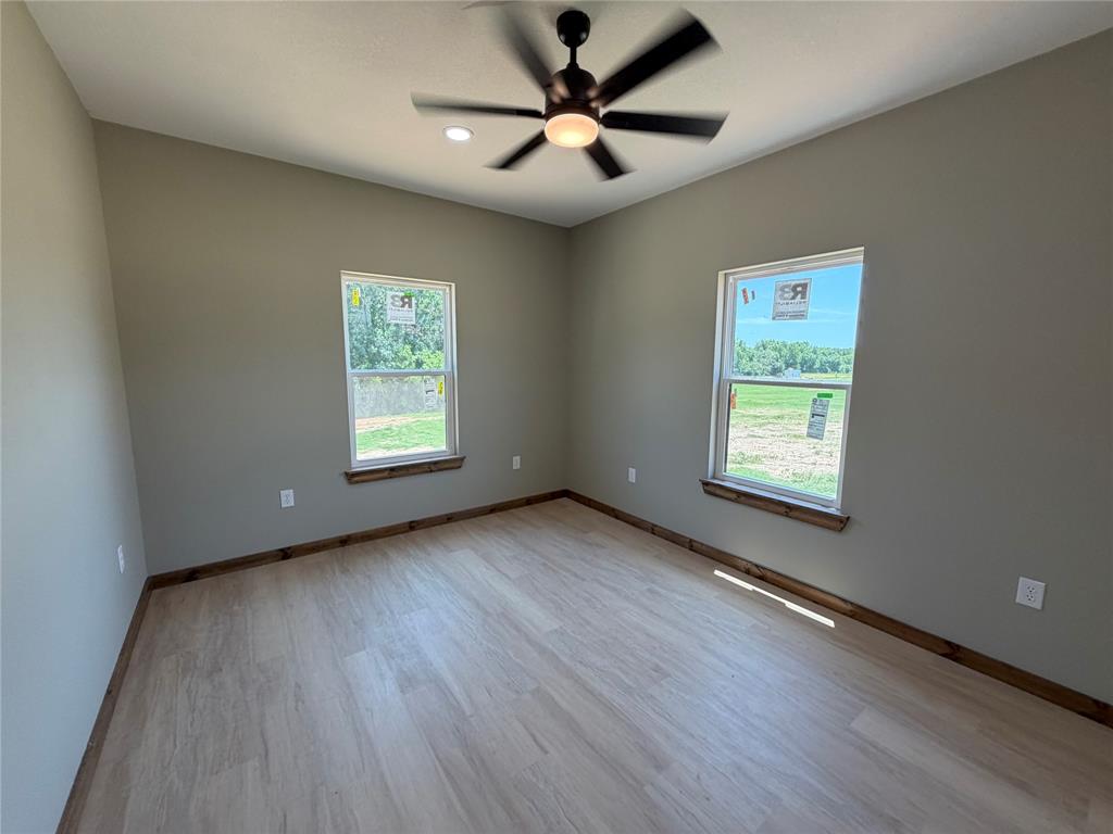1040 Rays Way Weatherford, TX 76085 - Photo 18 of 23 Neutral-toned bedroom featuring two windows, wood-finish flooring, and a ceiling fan with integrated lighting
