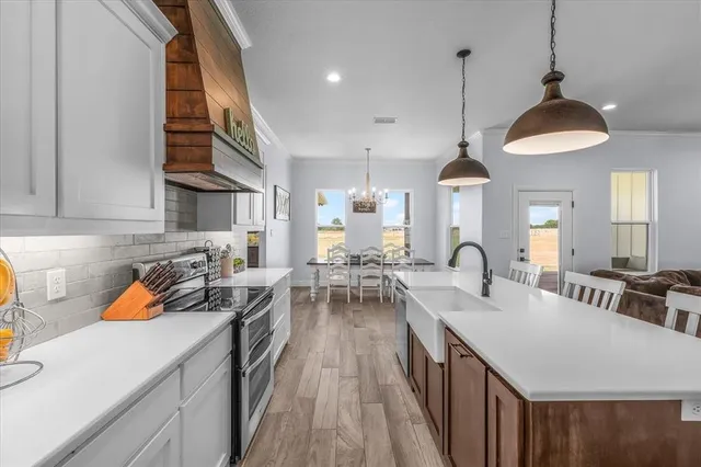 a kitchen with a stove a kitchen island a sink dishwasher a dining table and chairs with wooden floor