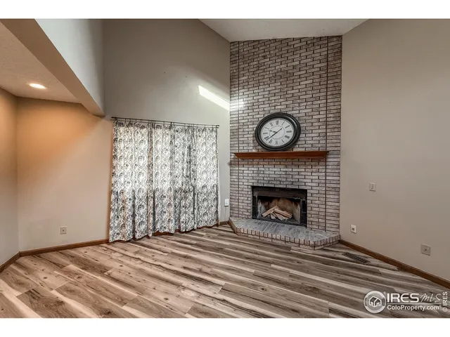 a view of an empty room with wooden floor fireplace and a window