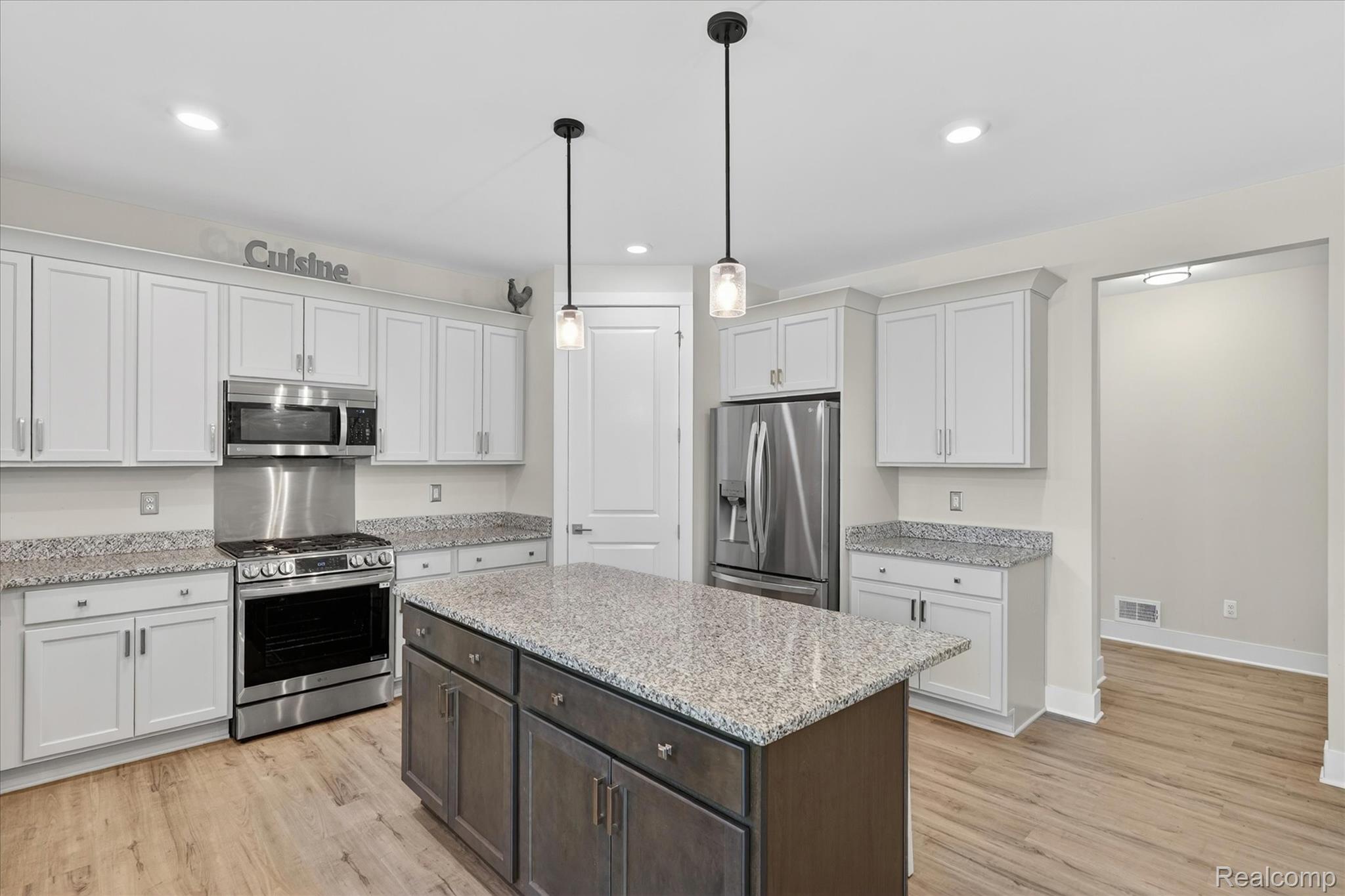 8130 Hinchey Road Pinckney, MI 48169 - Photo 13 of 62 Dual tone kitchen featuring stainless steel appliances, light wood-style flooring, dual tone cabinets, a center island, and light stone counters