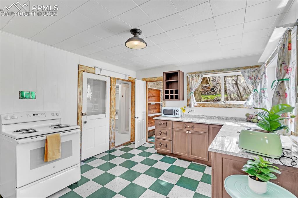 123 7th Street Victor, CO 80860 - Photo 32 of 50 Kitchen featuring white appliances, light flooring, open shelves, brown cabinets, and light stone counters