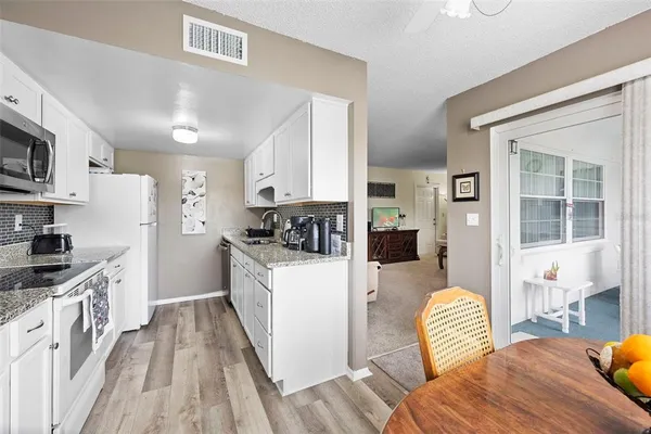 a kitchen with stainless steel appliances a refrigerator a stove a sink dishwasher and white cabinets with wooden floor