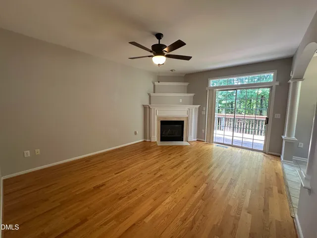 a view of an empty room with wooden floor fireplace and a window