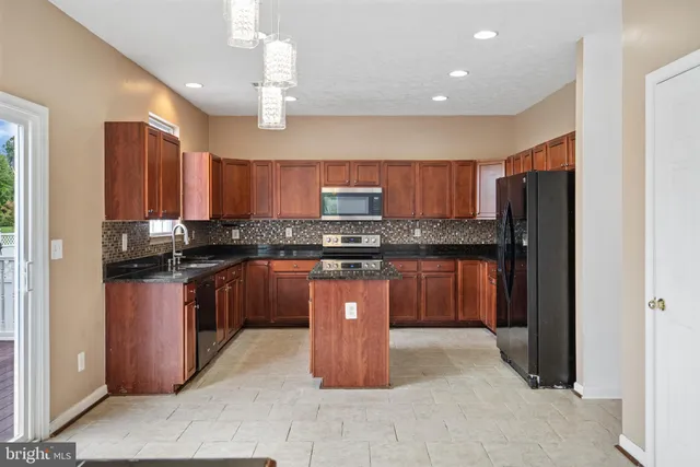 a kitchen with stainless steel appliances granite countertop wooden cabinets a refrigerator a sink a stove a microwave and a center island