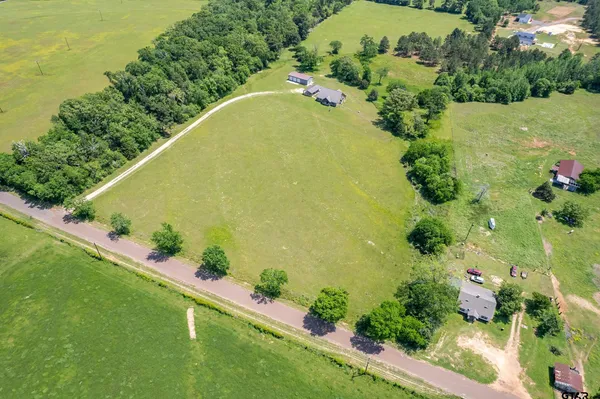 an aerial view of a residential houses with outdoor space and trees all around