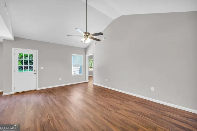 a view of an empty room with wooden floor and a ceiling fan