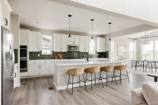 a large white kitchen with lots of counter space dining table and stainless steel appliances