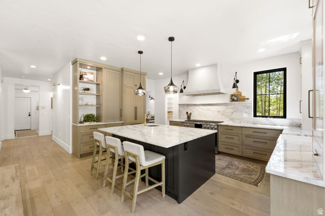 3027 Homestead Road Park City, UT 84098 - Photo 8 of 62 Gourmet kitchen featuring a large central island with seating, integrated appliances, natural wood-finish flooring, a contemporary range hood, and a striking black-framed window