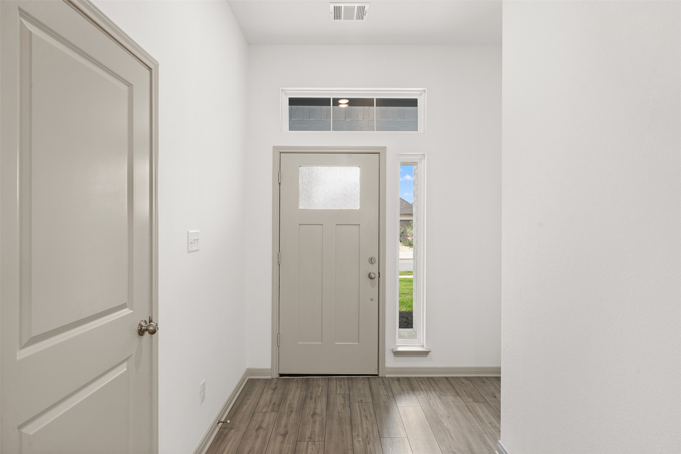 1968 Chief Street Bryan, TX 77807 - Photo 19 of 27 This entryway features a modern front door with frosted glass for privacy, complemented by a horizontal and vertical window for natural light. The space has sleek, wood-look flooring and neutral walls, creating a bright, welcoming atmosphere.