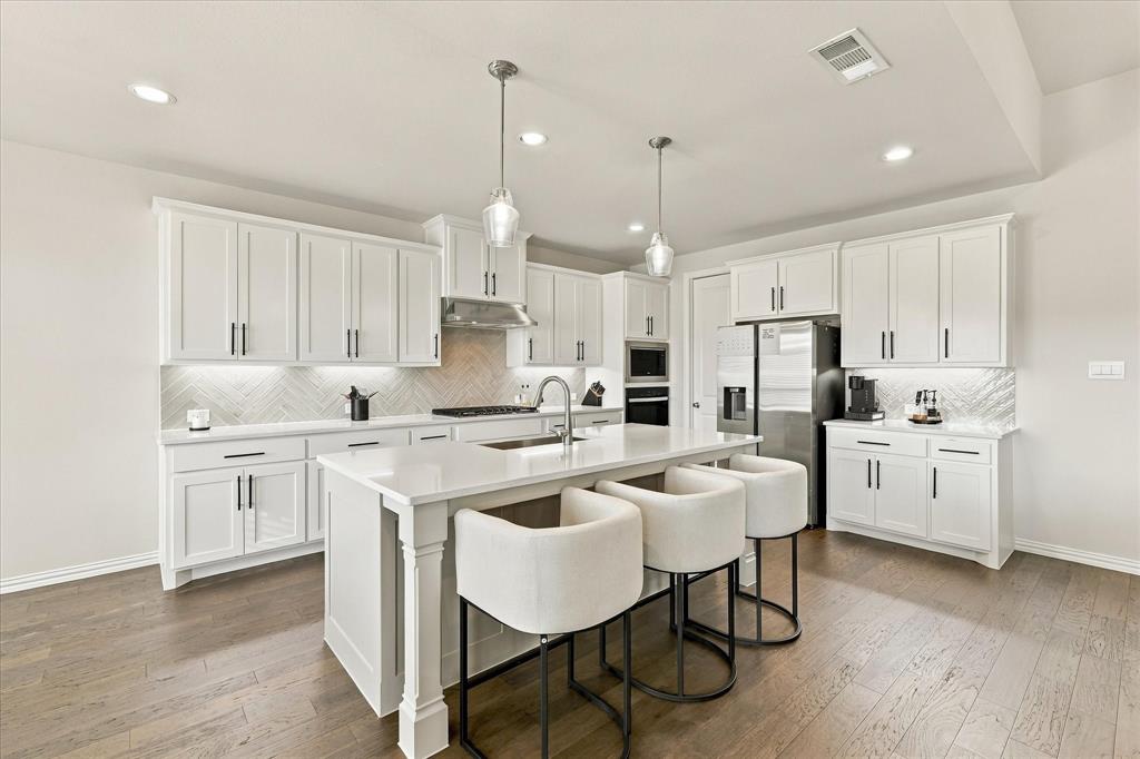137 Chisos Court Rhome, TX 76078 - Photo 17 of 40 Bright kitchen featuring white shaker cabinetry, an island with solid surface countertops, stainless steel appliances, wood-finish flooring, and recessed lighting