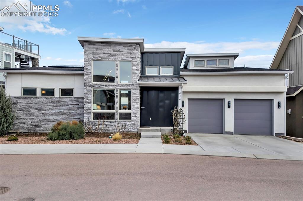 View of front of property featuring stone siding, driveway, stucco siding, and an attached garage