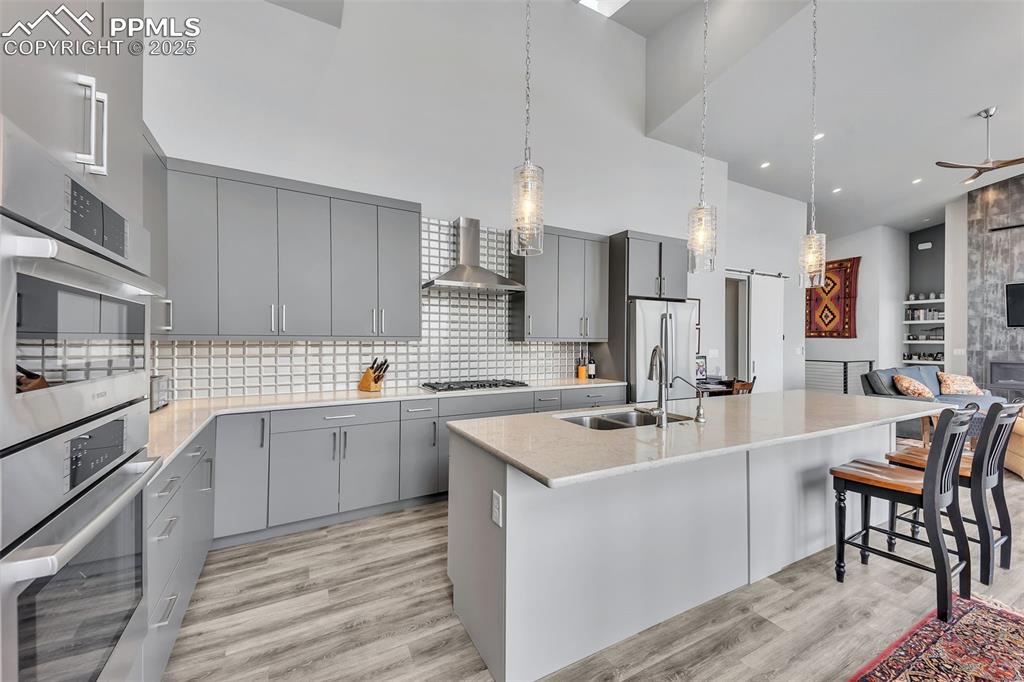 414 Eclipse Drive Colorado Springs, CO 80905 - Photo 8 of 50 Kitchen with gray cabinetry, wall chimney exhaust hood, light wood-style flooring, and appliances with stainless steel finishes