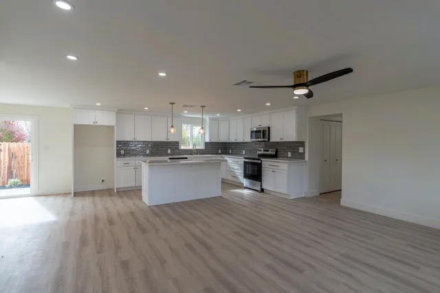 a large kitchen with kitchen island a stove a sink dishwasher a refrigerator and white cabinets with wooden floor