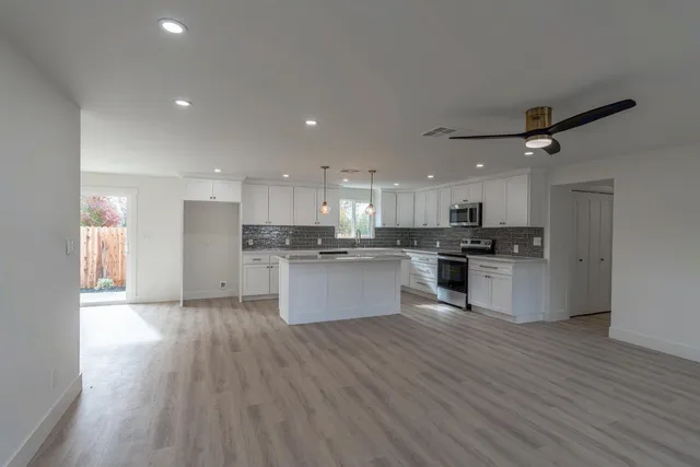 a large kitchen with kitchen island a stove a sink dishwasher a refrigerator and white cabinets with wooden floor