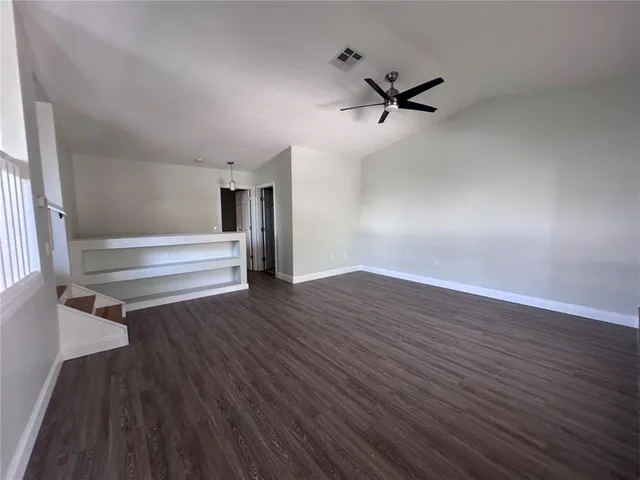 an empty room with wooden floor a ceiling fan and windows