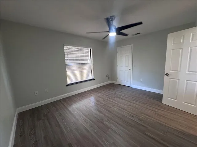 an empty room with wooden floor a ceiling fan and windows