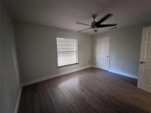 an empty room with wooden floor a ceiling fan and windows