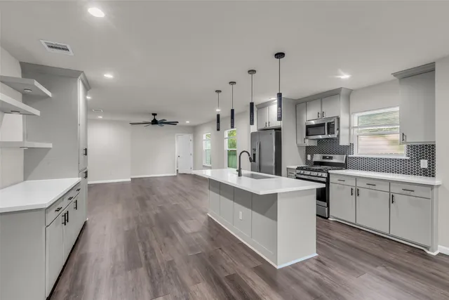 a large kitchen with granite countertop a large stove a sink dishwasher a refrigerator and white cabinets with wooden floor