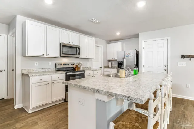 a kitchen with stainless steel appliances granite countertop a stove top oven a sink a dining table and chairs with wooden floor