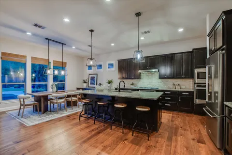 a kitchen with stainless steel appliances granite countertop a refrigerator a stove top oven a sink dishwasher a dining table and chairs with wooden floor