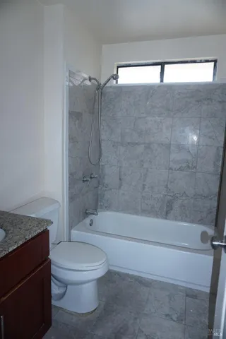 a bathroom with a granite countertop bathtub shower sink vanity and toilet