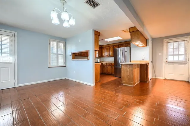 an empty room with wooden floor a chandelier fan and windows
