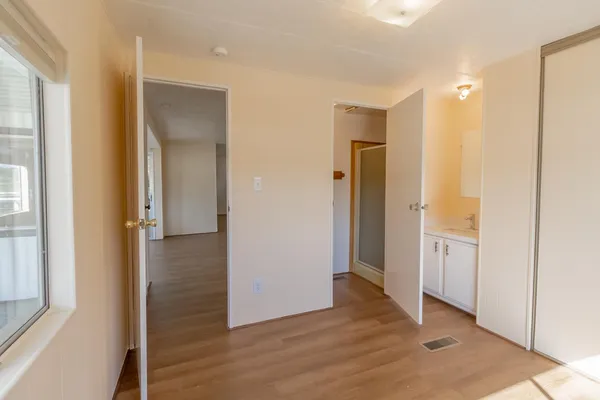 a view of an empty room with wooden floor and a bathroom