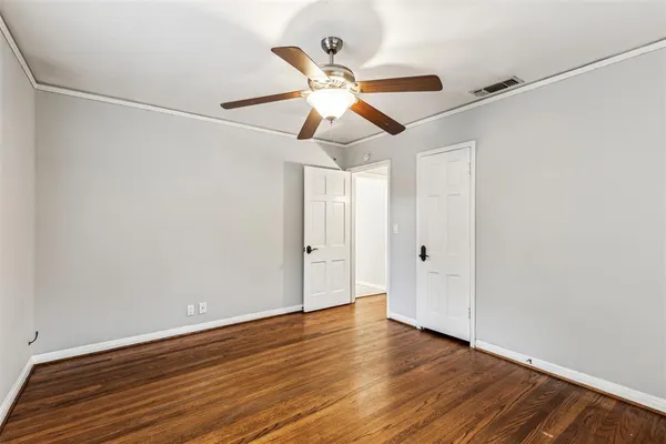 a view of an empty room with wooden floor and a ceiling fan