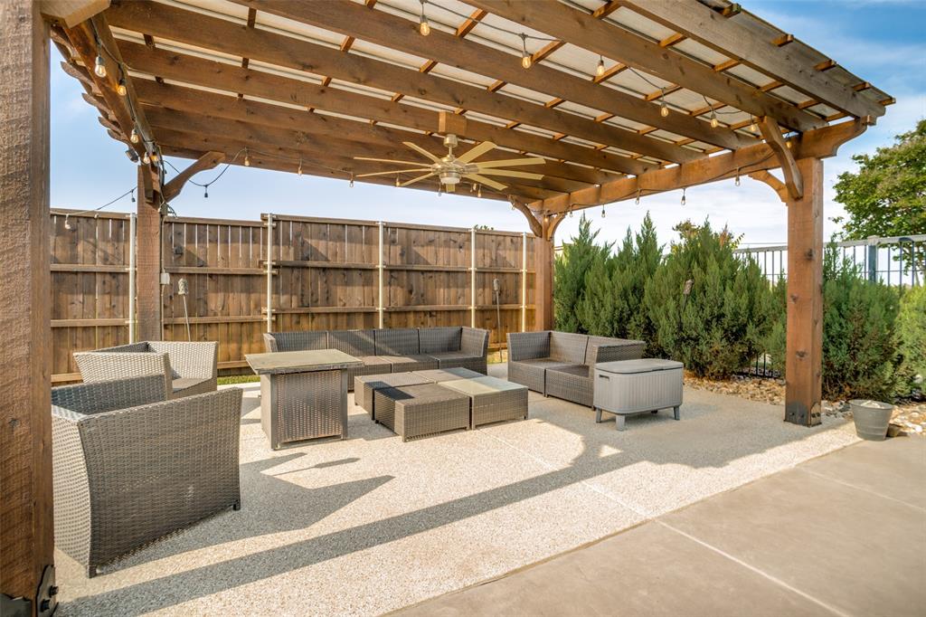 1461 Ramsbury Lane Prosper, TX 75078 - Photo 25 of 30 Expansive outdoor patio featuring a wooden pergola with string lights and a ceiling fan, a gravel-covered surface, mature shrubs, and a wood fence enclosure
