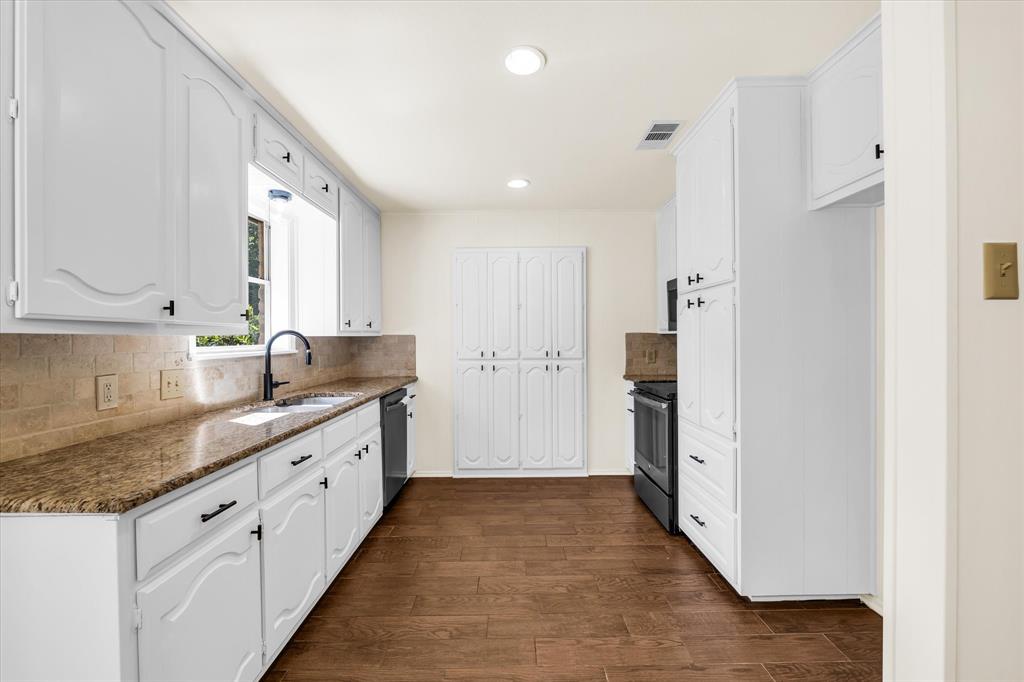 141 Travis Lane Hewitt, TX 76643 - Photo 12 of 31 Kitchen featuring wood-finish flooring, white cabinetry with dark hardware, stone-look countertops, and a tile backsplash