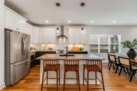 a kitchen with stainless steel appliances a dining table chairs refrigerator and wooden floor