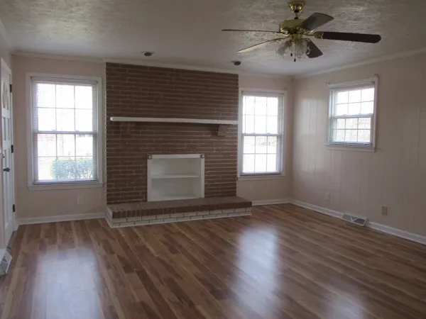 an empty room with wooden floor fan and windows