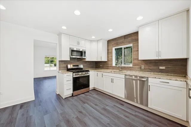 a kitchen with granite countertop a stove top oven a sink dishwasher and a refrigerator with wooden floor