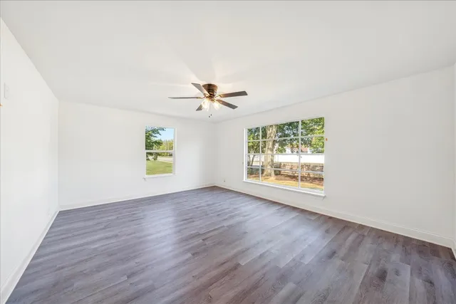 an empty room with wooden floor chandelier fan and windows