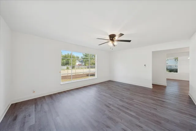 an empty room with wooden floor chandelier fan and windows
