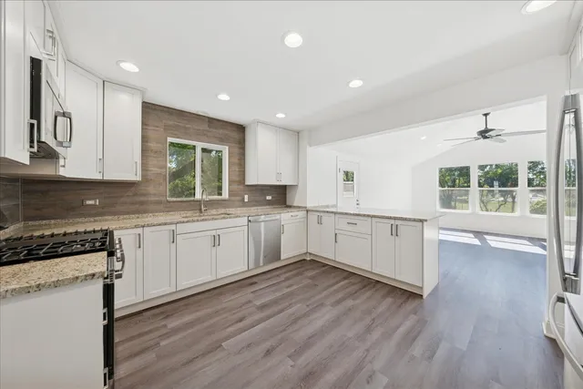 a large kitchen with stainless steel appliances granite countertop a stove a sink and white cabinets with wooden floor