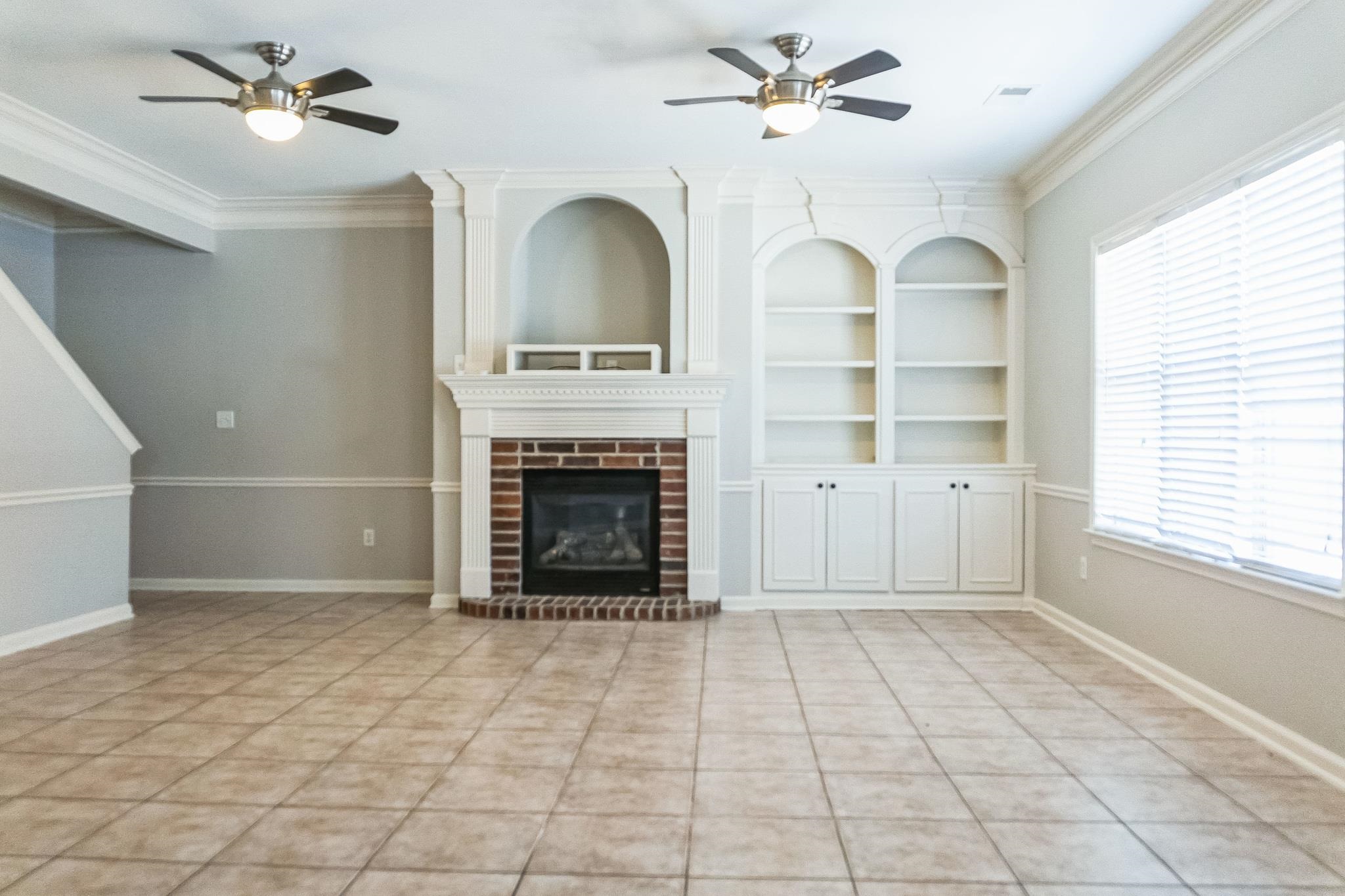 5225 Rockyford Road Bartlett, TN 38002 - Photo 5 of 18 Unfurnished living room featuring a healthy amount of sunlight, a brick fireplace, crown molding, and built in shelves