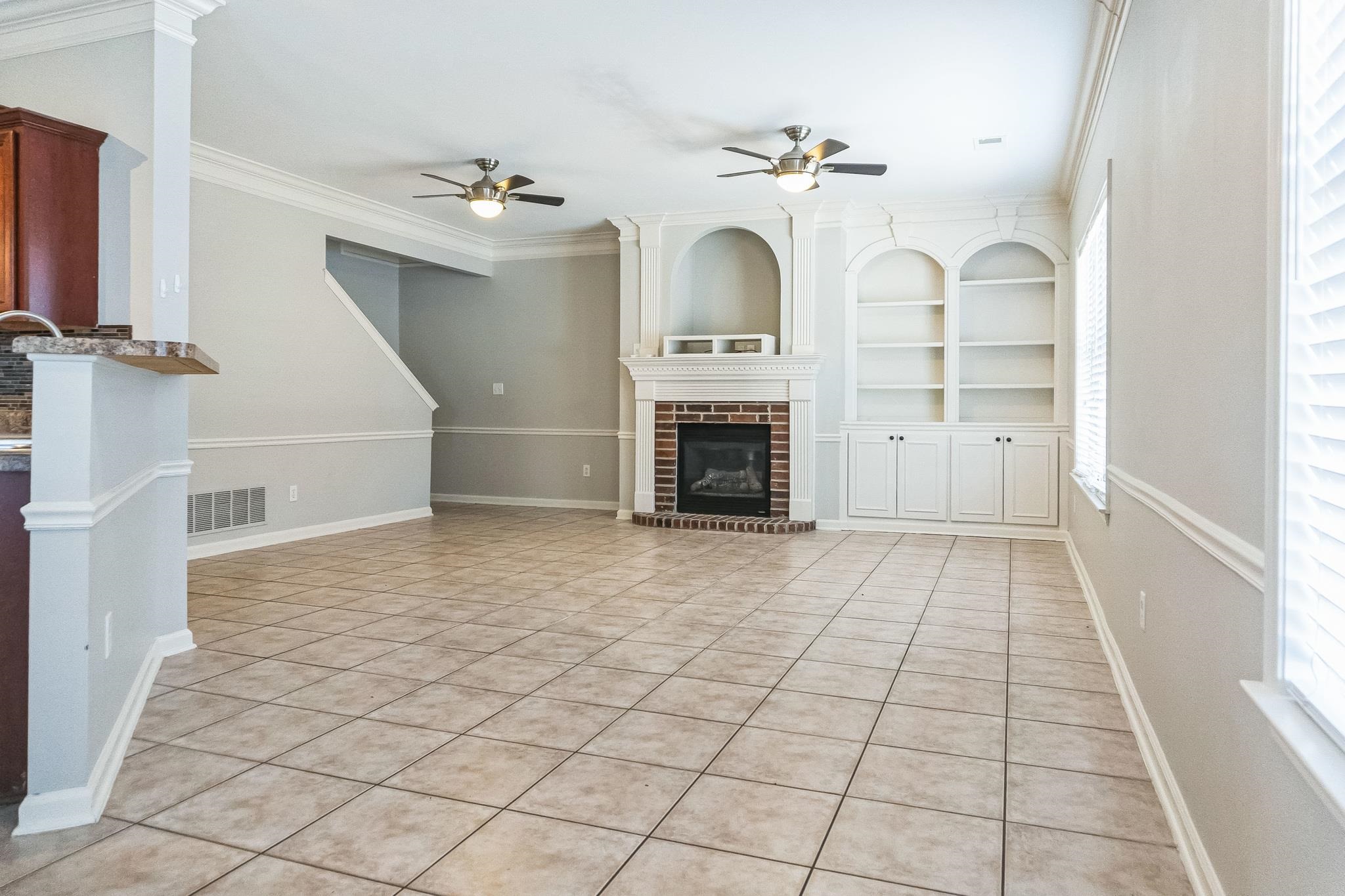 5225 Rockyford Road Bartlett, TN 38002 - Photo 7 of 18 Unfurnished living room with ornamental molding, light tile patterned floors, a fireplace, built in features, and ceiling fan