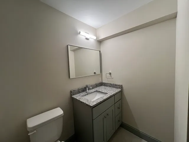 a bathroom with a granite countertop sink toilet and mirror