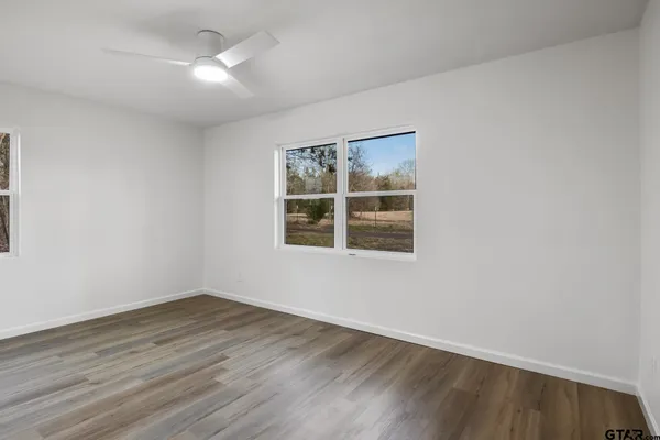 a view of an empty room with wooden floor and a kitchen