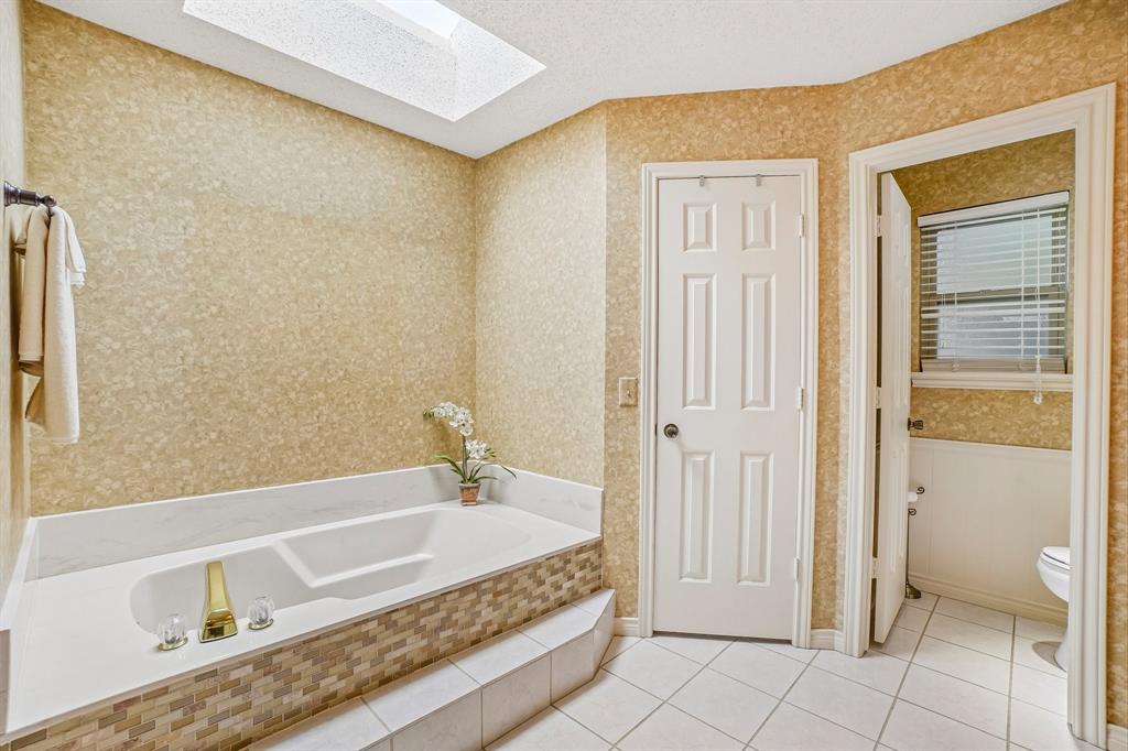 12929 Jasoncrest Trail Dallas, TX 75243 - Photo 25 of 38 Soaking tub with a tiled surround and steps, illuminated by a ceiling skylight