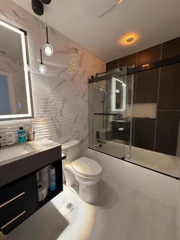 a bathroom with a granite countertop sink a toilet a mirror and shower