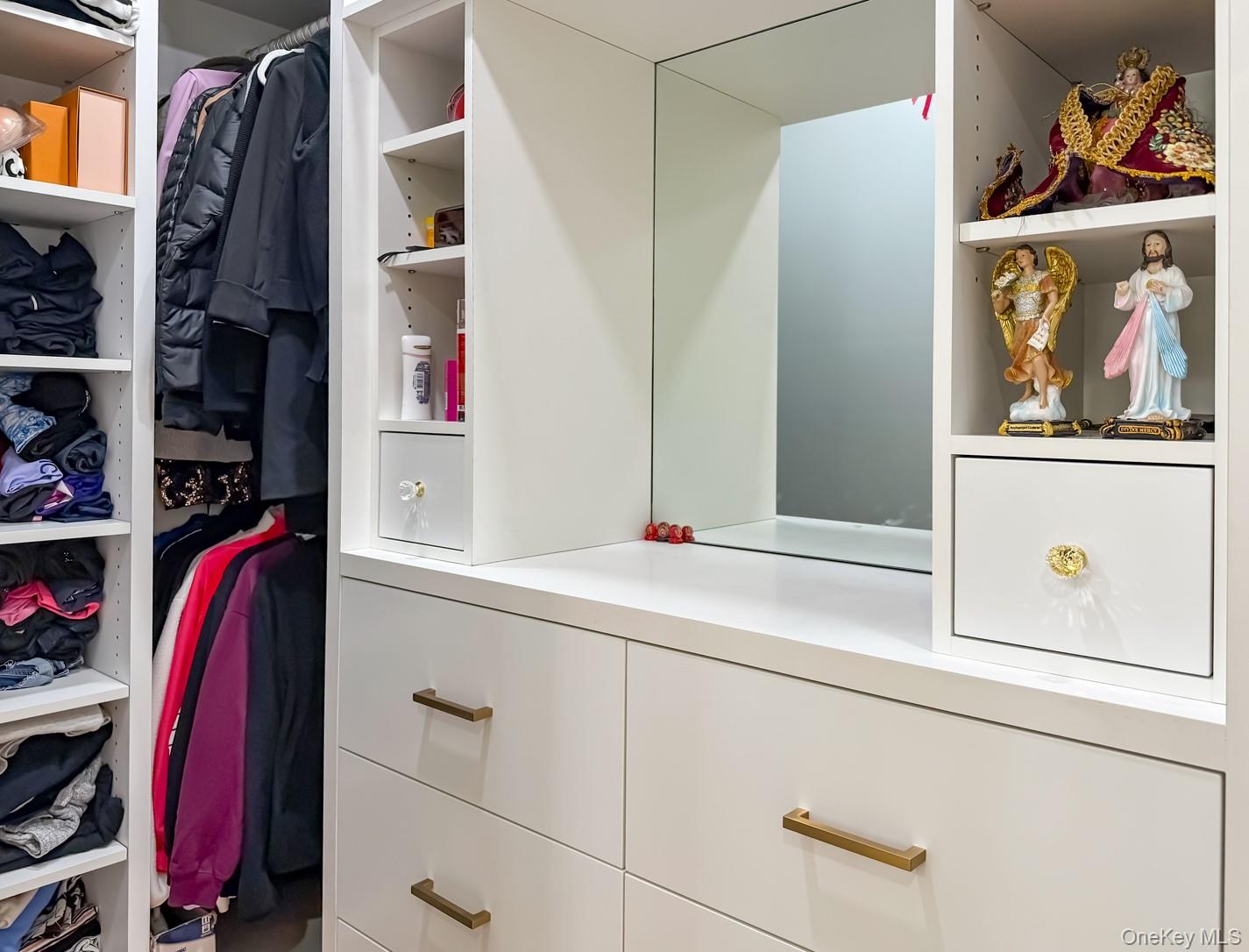 49 Meadow Road Montrose, NY 10548 - Photo 20 of 50 Custom closet system featuring white cabinetry, built-in shelving, hanging storage, integrated drawers with brass-finish hardware, and a vanity mirror