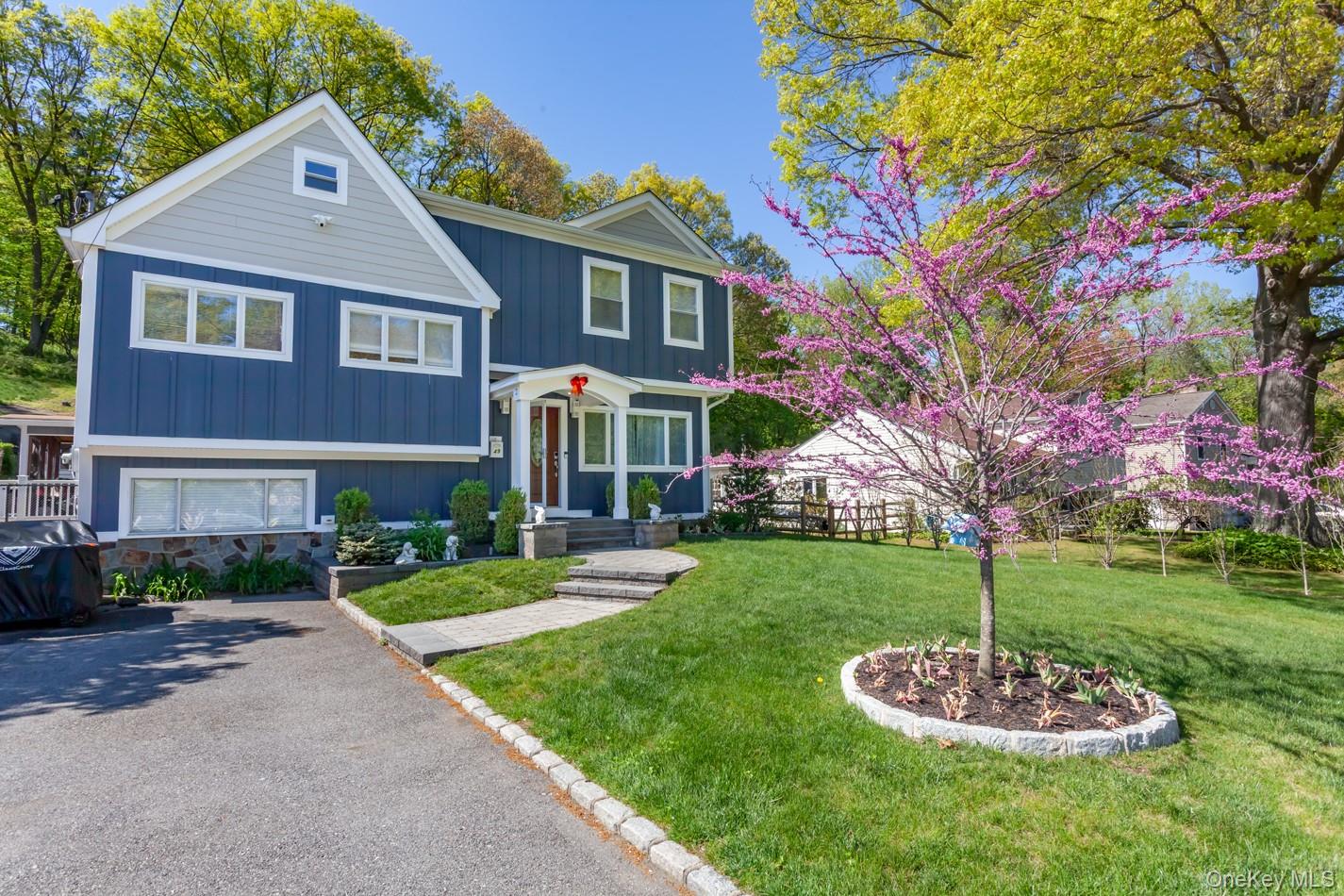 49 Meadow Road Montrose, NY 10548 - Photo 3 of 50 Blue siding exterior with white trim, a stone foundation, a paved driveway, a stone walkway, and a manicured lawn with a blooming tree
