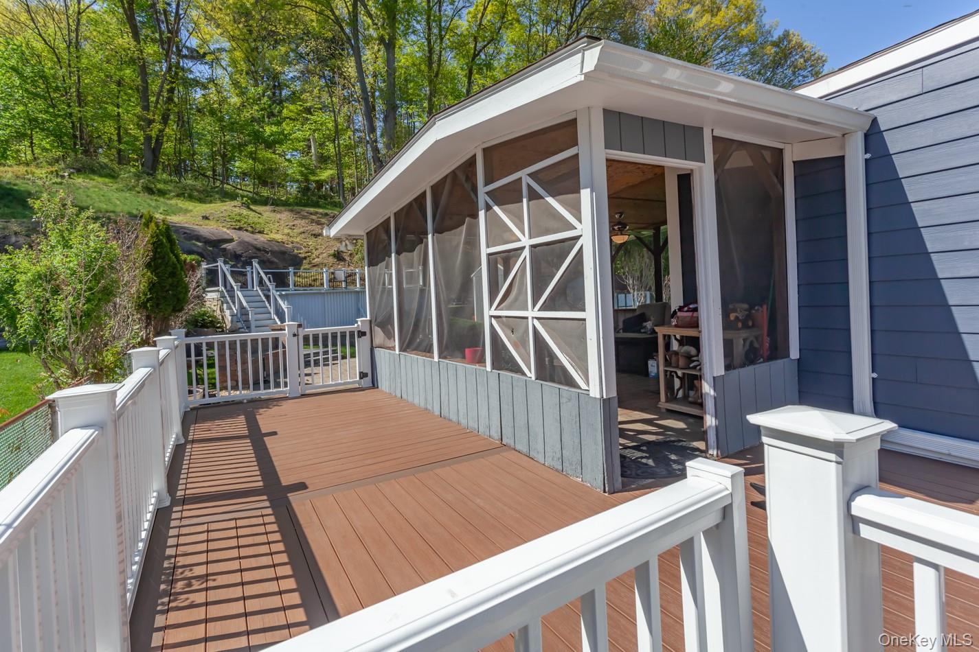 49 Meadow Road Montrose, NY 10548 - Photo 40 of 50 Expansive wood-finish deck with white railing system and gate, providing direct access to a screened-in porch with a ceiling fan