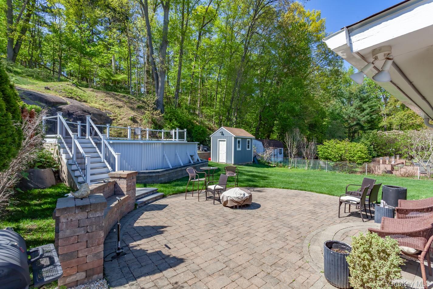 49 Meadow Road Montrose, NY 10548 - Photo 41 of 50 Expansive paver patio with a built-in stone feature, overlooking a manicured lawn, an above-ground pool with deck access, and a storage shed