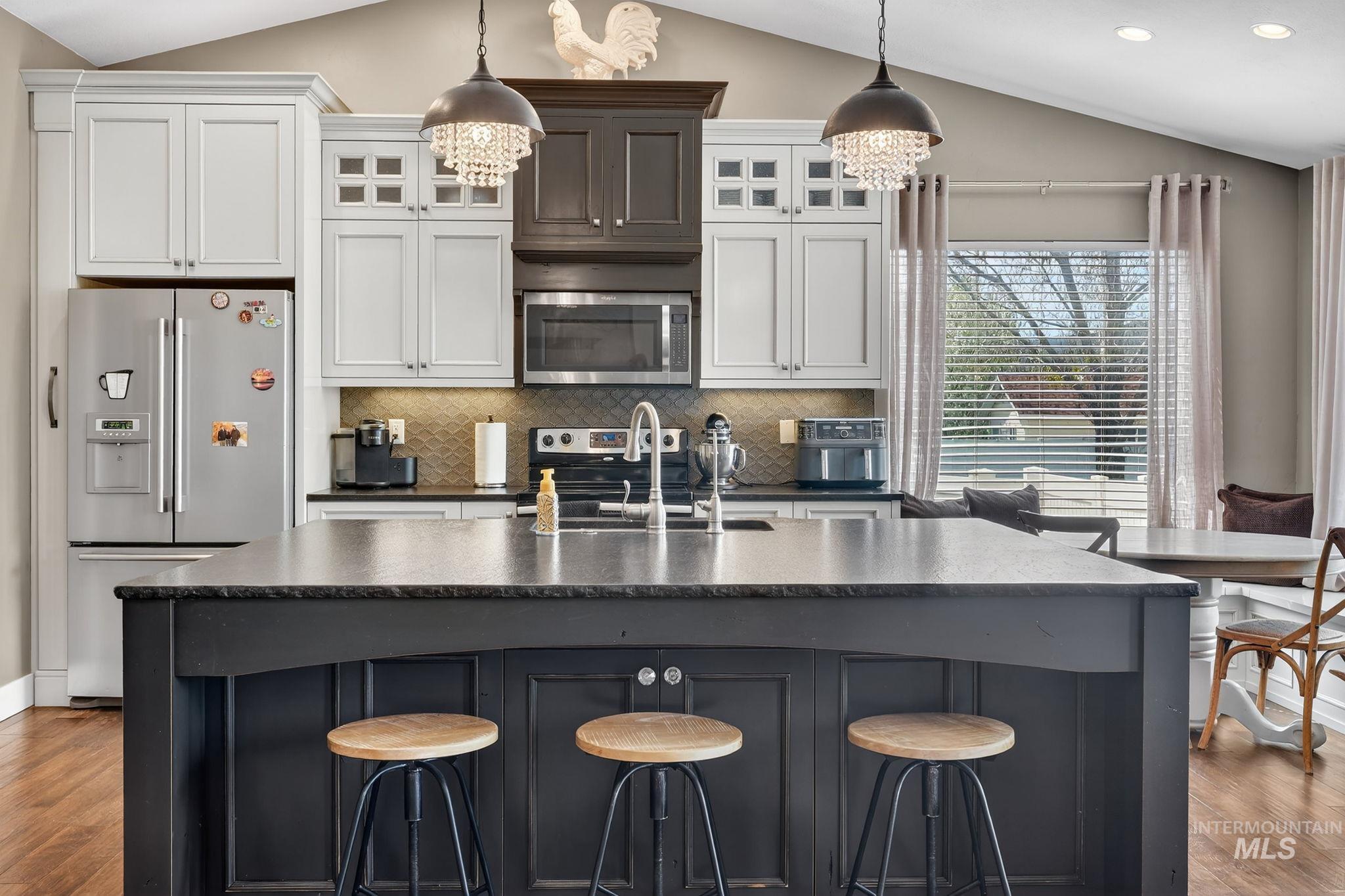 880 Redman Street Chubbuck, ID 83202 - Photo 7 of 39 Kitchen with dark wood-type flooring, stainless steel appliances, vaulted ceiling, glass insert cabinets, and a center island with sink